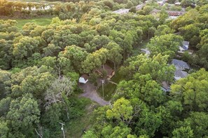 An aerial view of a residential area with dense greenery, houses, and a small white building. - Spacious 3BR House With Firepit & Grill, Near Beach (Gary)