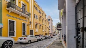 A narrow cobblestone street lined with colorful buildings, parked cars, and a gated entrance. - Loft La Luz - Old San Juan (San Juan)