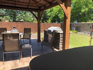 Un patio al aire libre con una parrilla, sillas y una mesa.