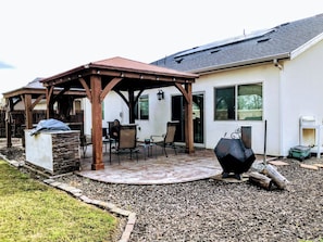 Ein überdachter Patio-Bereich mit Gartenmöbeln, einem Grill und einem Steinpflanzgefäß.