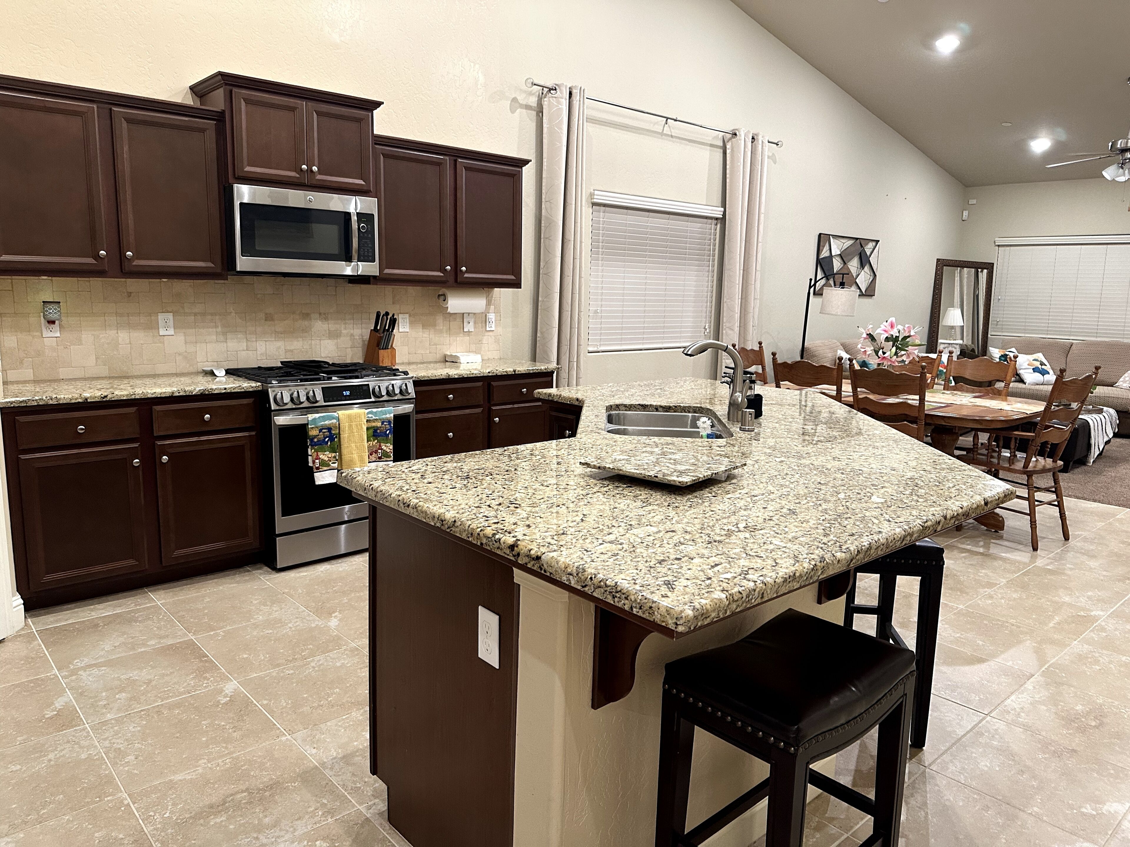 A modern kitchen with dark brown cabinets, a granite countertop, a stainless steel oven, and a dining area with a wooden table and chairs.