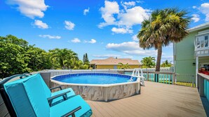Una piscina con muelle de madera, una silla de descanso y una palmera.