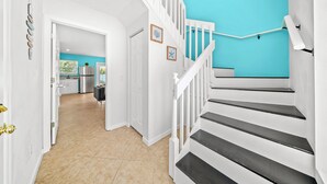 Una escalera con barandillas blancas y peldaños negros que lleva a una habitación con pared turquesa.