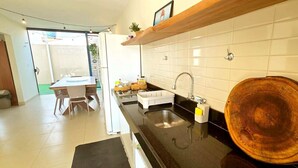 A modern kitchen with a black countertop, white tiles, and a wooden shelf. - Refúgio Praiano do Atalaia (Salinópolis)