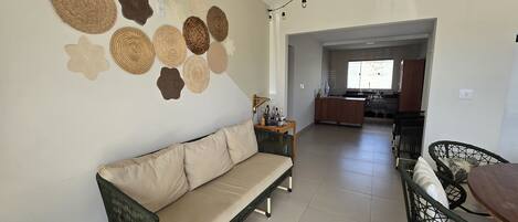 A living room with a sofa, a dining table with chairs, a kitchen area, and a wall decorated with woven baskets.
