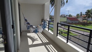 A balcony with a hammock, a view of a road, and buildings in the background. - Refúgio Praiano do Atalaia (Salinópolis)