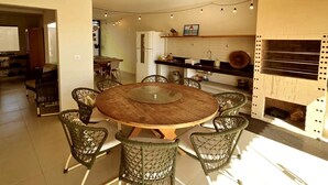 A modern kitchen with a round wooden table surrounded by wireframe chairs, a built-in oven, and pendant lighting. - Refúgio Praiano do Atalaia (Salinópolis)