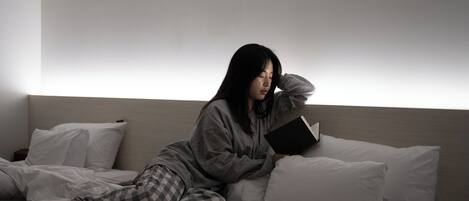 A person sitting on a bed in a room with a plain wall and a nightstand.