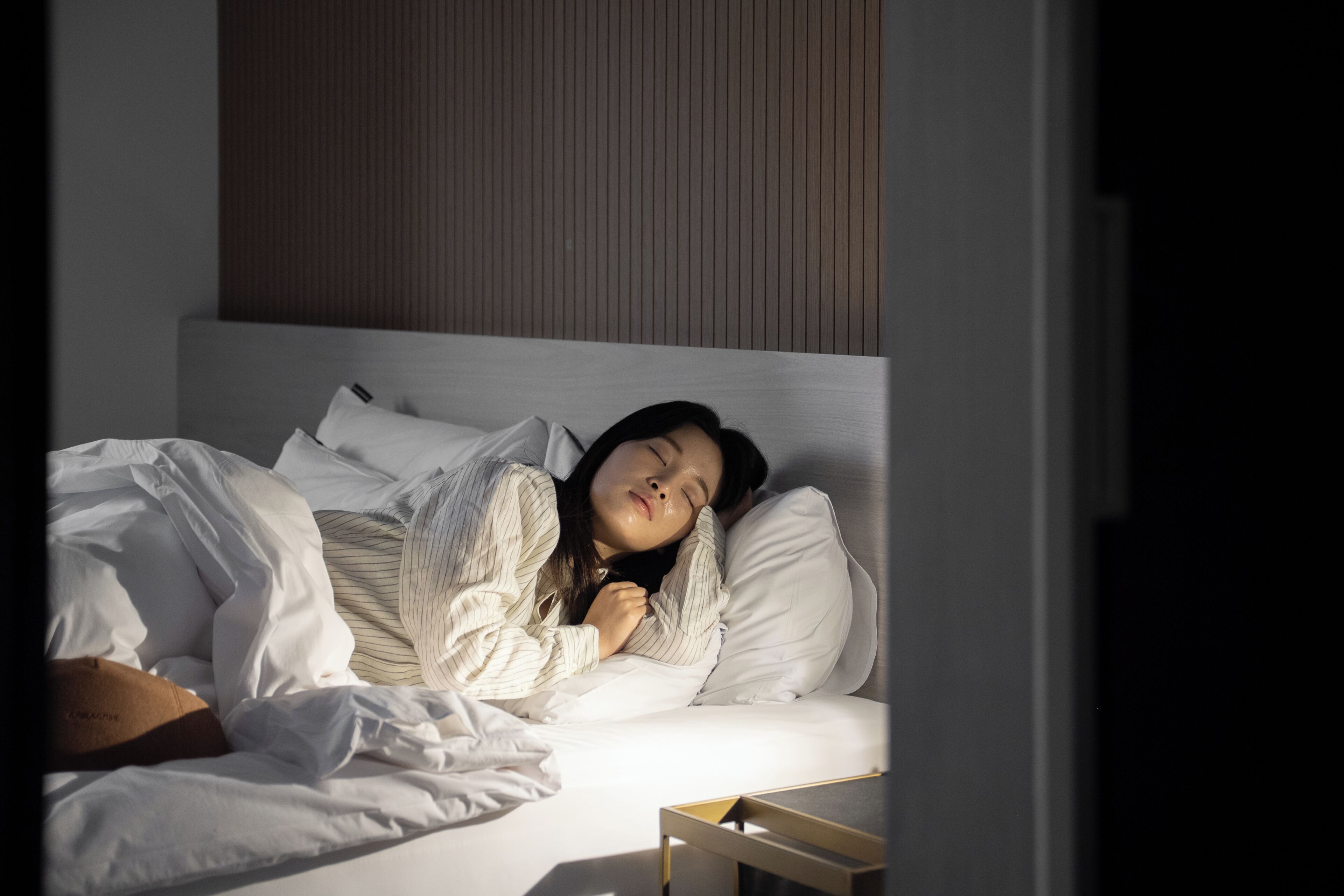 Una persona durmiendo en una cama con ropa de cama blanca y un cabecero de madera.