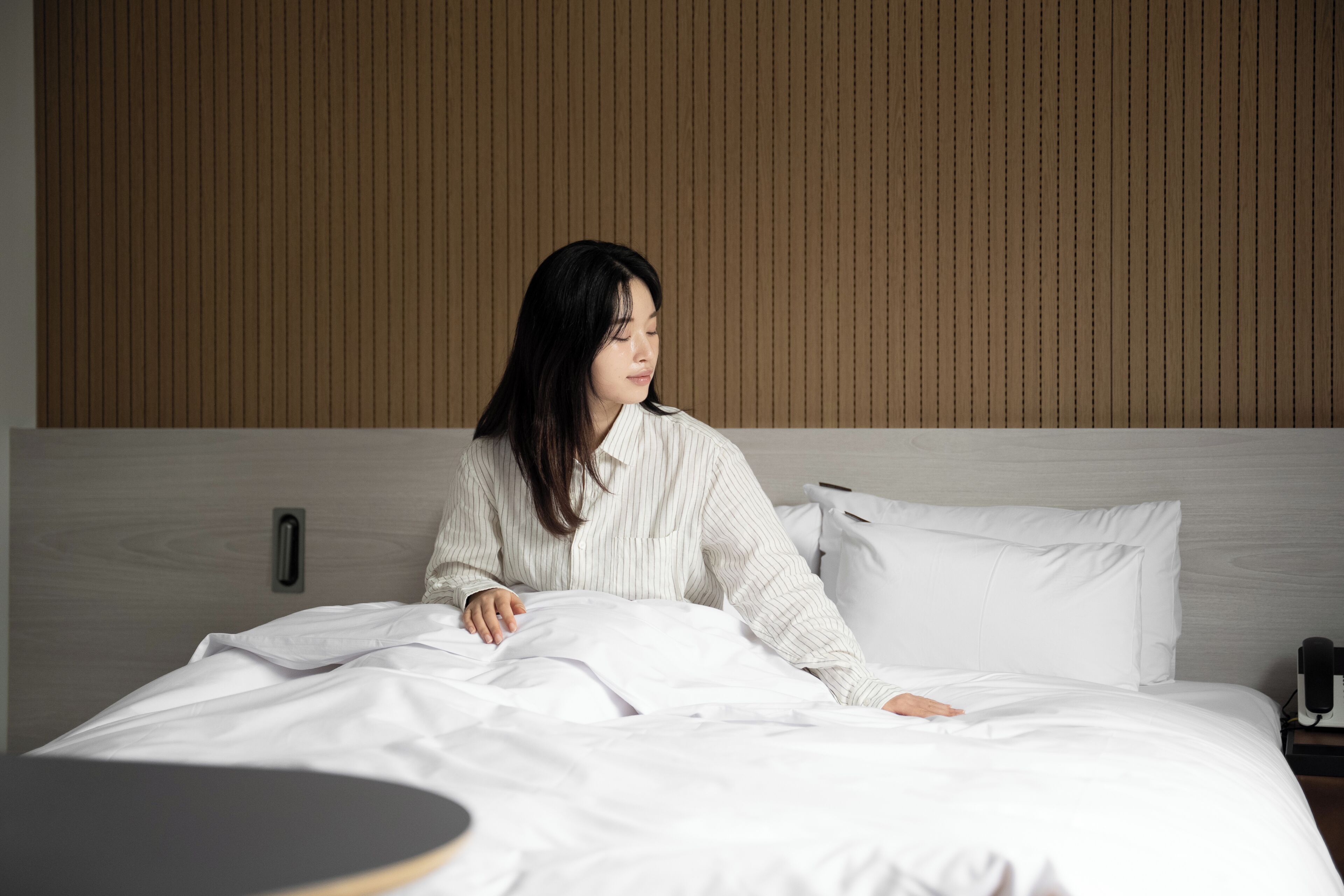 A hotel room with a bed, a bedside table, and a wall with vertical lines.