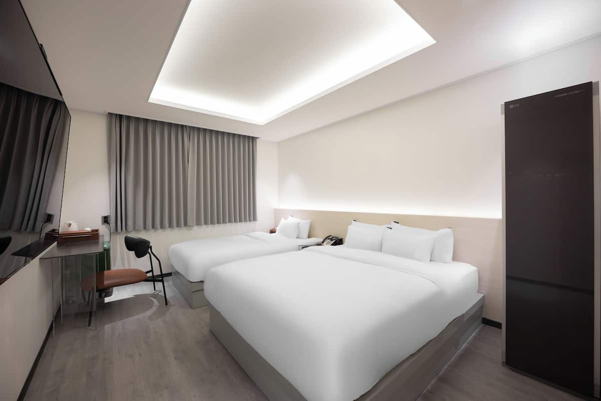 A hotel room with two beds, a desk, a chair, a wardrobe, and a ceiling light.