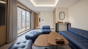 Ein modernes Hotelzimmer mit großem Fenster, einer Couch, einem Couchtisch und einem Flachbildfernseher.