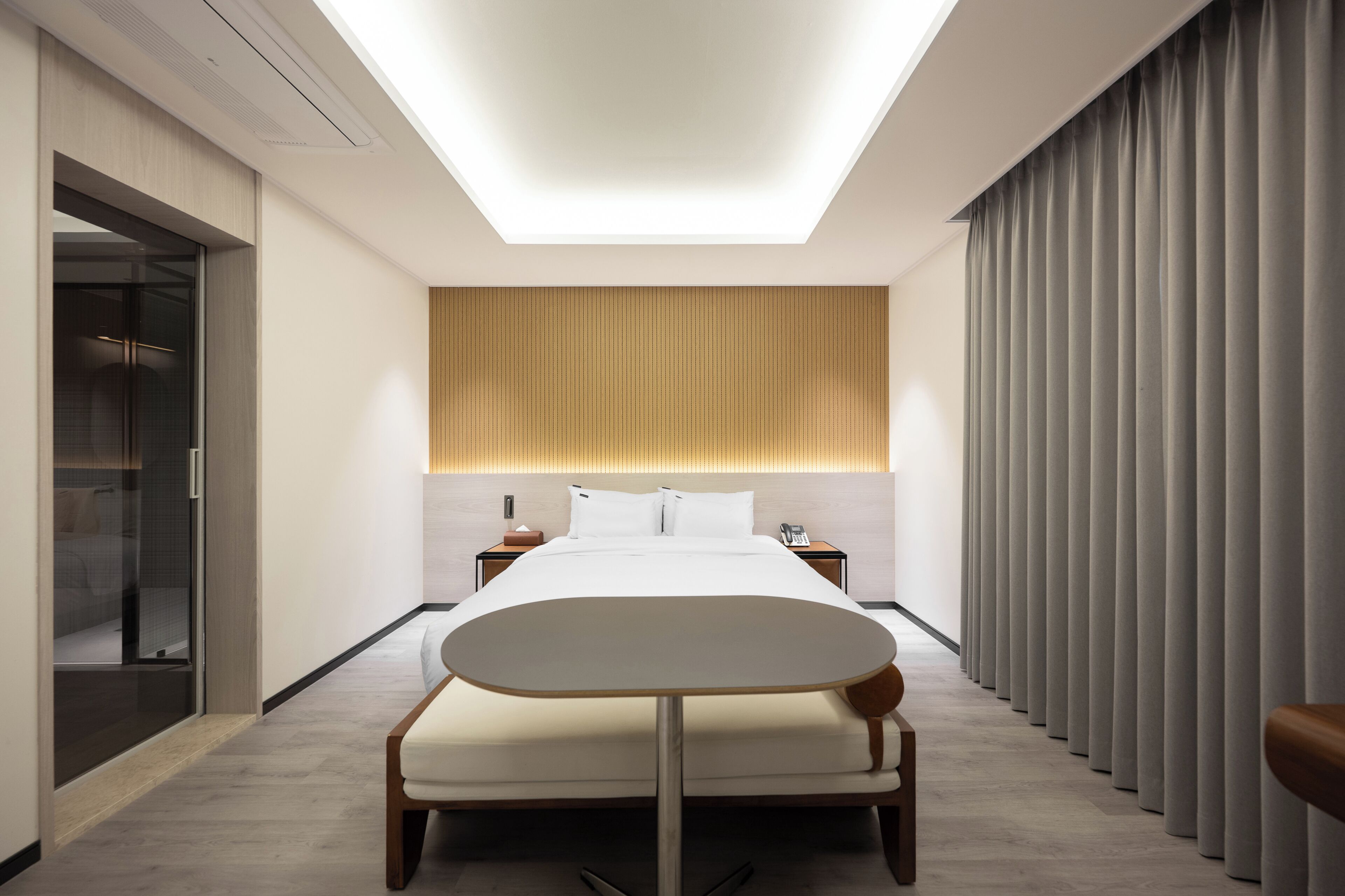 A modern hotel room with a bed, bedside tables, a small table, a mirror, and a sliding door.