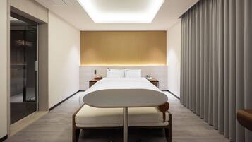 A modern hotel room with a bed, bedside tables, a small table, a mirror, and a sliding door.