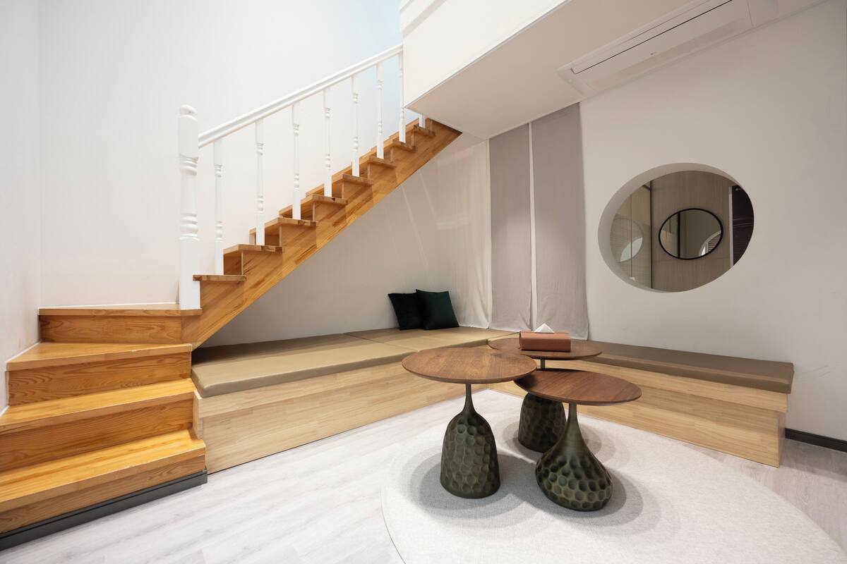 A modern interior with a wooden staircase, a round mirror, and two textured tables.