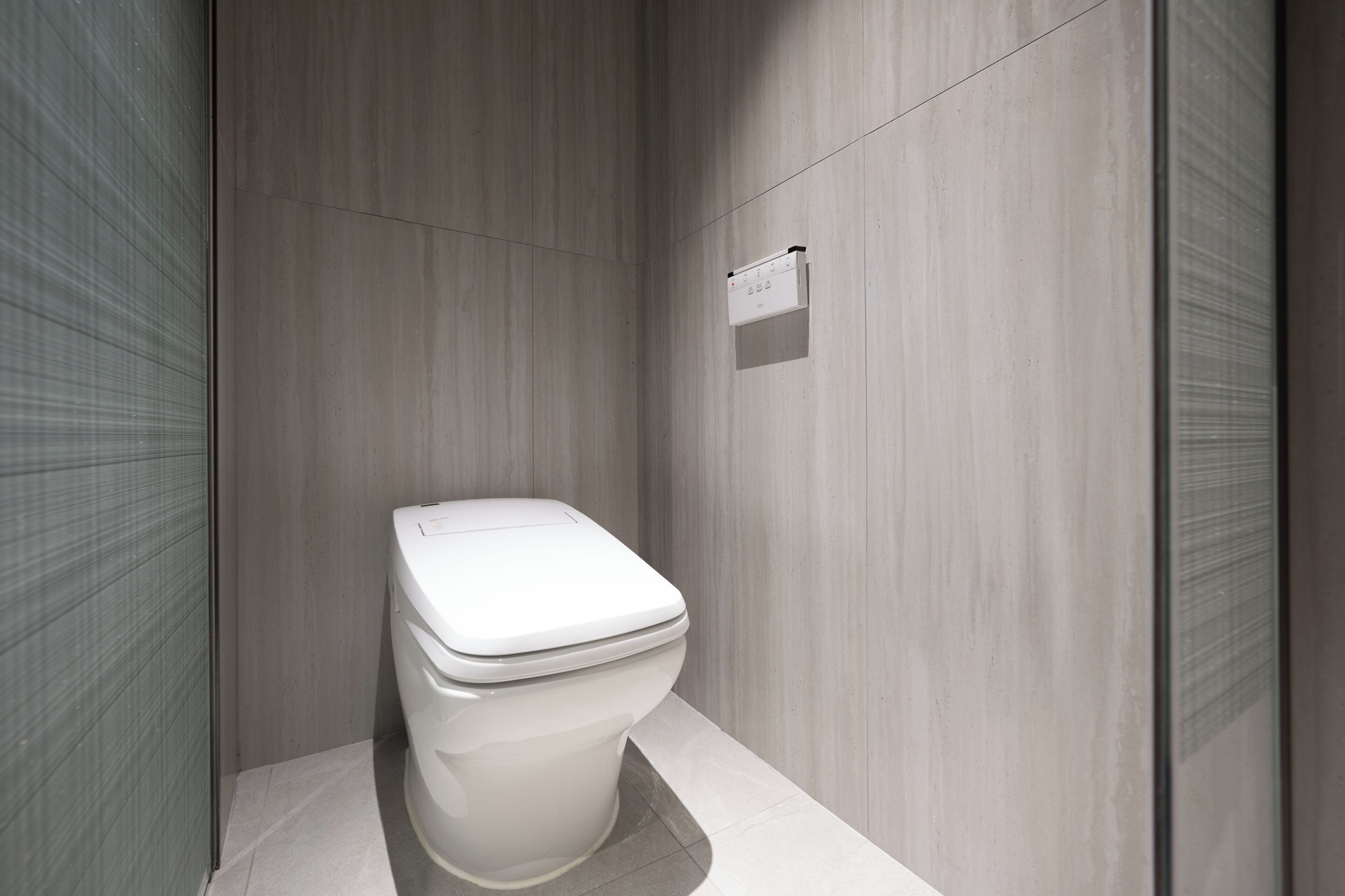 Un baño moderno con inodoro blanco, panel de control en la pared y suelo de baldosas.