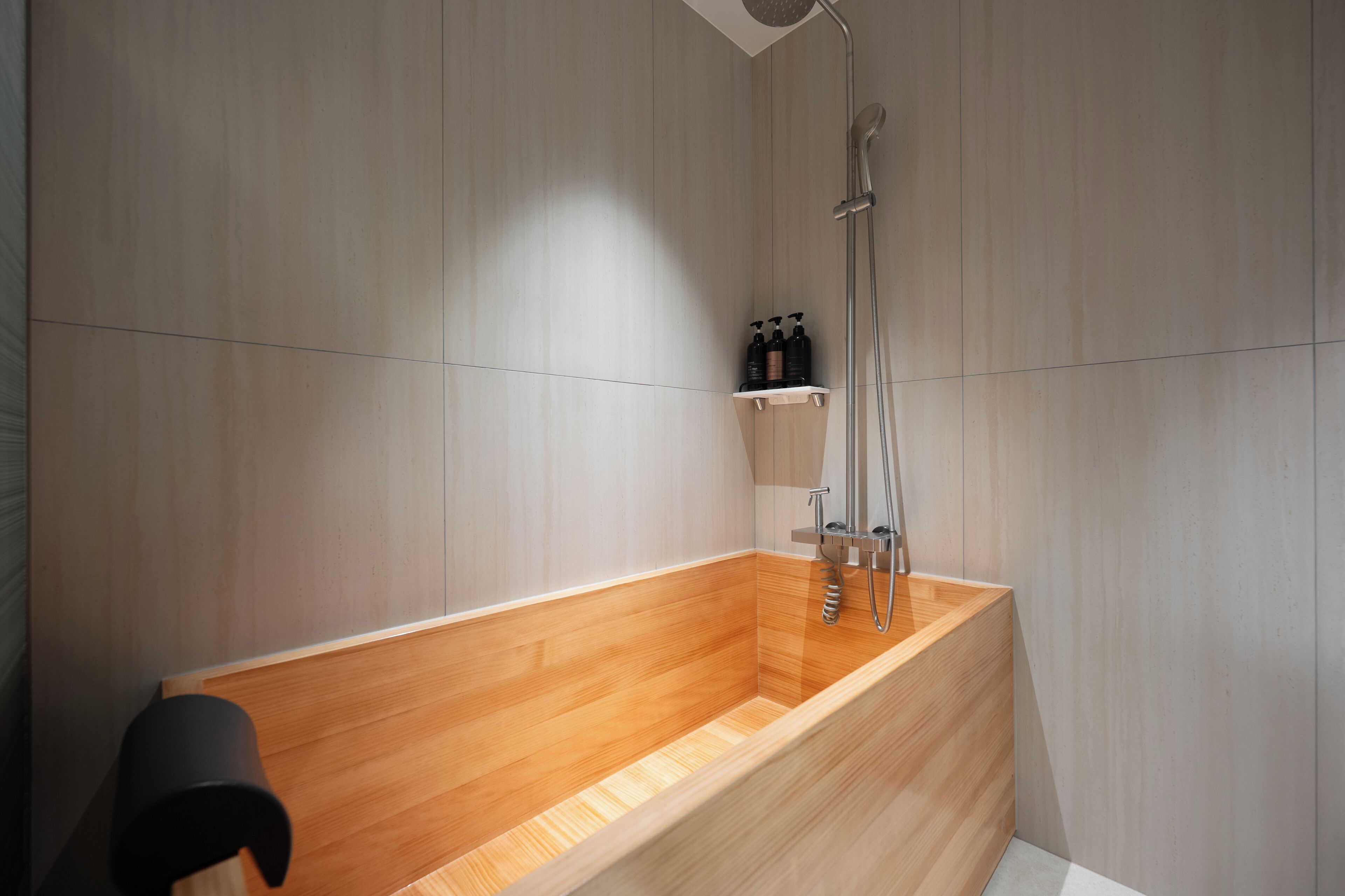 A modern bathroom with a wooden bathtub, a shower, and a shelf with toiletries.