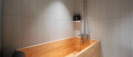 A modern bathroom with a wooden bathtub, a shower, and a shelf with toiletries.