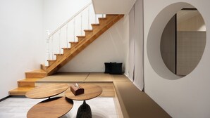 Ein modernes Interieur mit einer Holztreppe, einem runden Spiegel und einer Sitzecke mit einem kleinen Tisch.