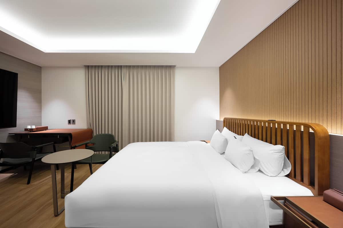 A modern hotel room with a large bed, a desk, a chair, and a small table.
