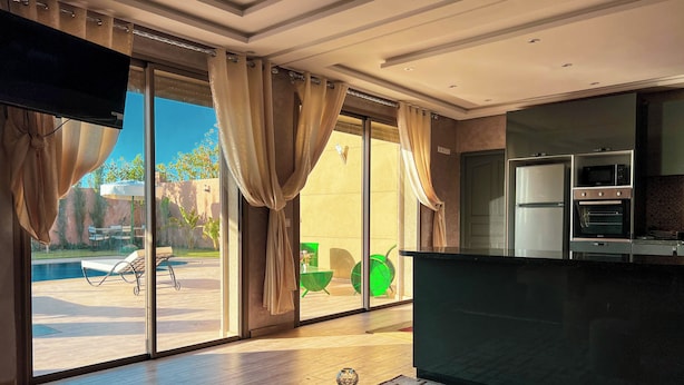 A modern kitchen with built-in appliances, a dining area with a wooden table and ottomans, and large sliding glass doors leading to a pool area. - 3-bedroom Luxury Villa with Private Pool (Taht Eddoum)