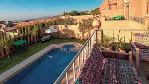 A pool area with a view of a desert landscape, a covered seating area, and a building with a unique architectural style. - 3-bedroom Luxury Villa with Private Pool (Taht Eddoum)