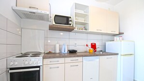 Una cocina compacta con armarios blancos, estufa, microondas, lavavajillas y refrigerador.
