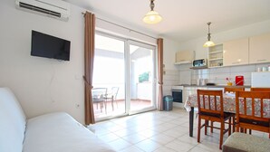 Una habitación con cama, una mesa de comedor con sillas, una zona de cocina y un ventanal corredero que da a un patio exterior.