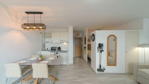 Uma cozinha moderna com armários brancos, uma área de refeições com mesa e cadeiras, e um corredor que dá para um quarto.