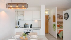 Uma cozinha moderna com armários brancos, micro-ondas e uma sala de jantar com mesa e cadeiras de vidro.