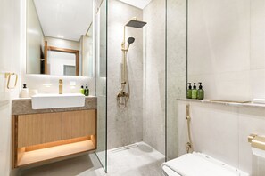 A modern bathroom with a glass-enclosed shower, a wooden vanity, and a large mirror. - Spacious Modern Studio in JVC (Dubai)