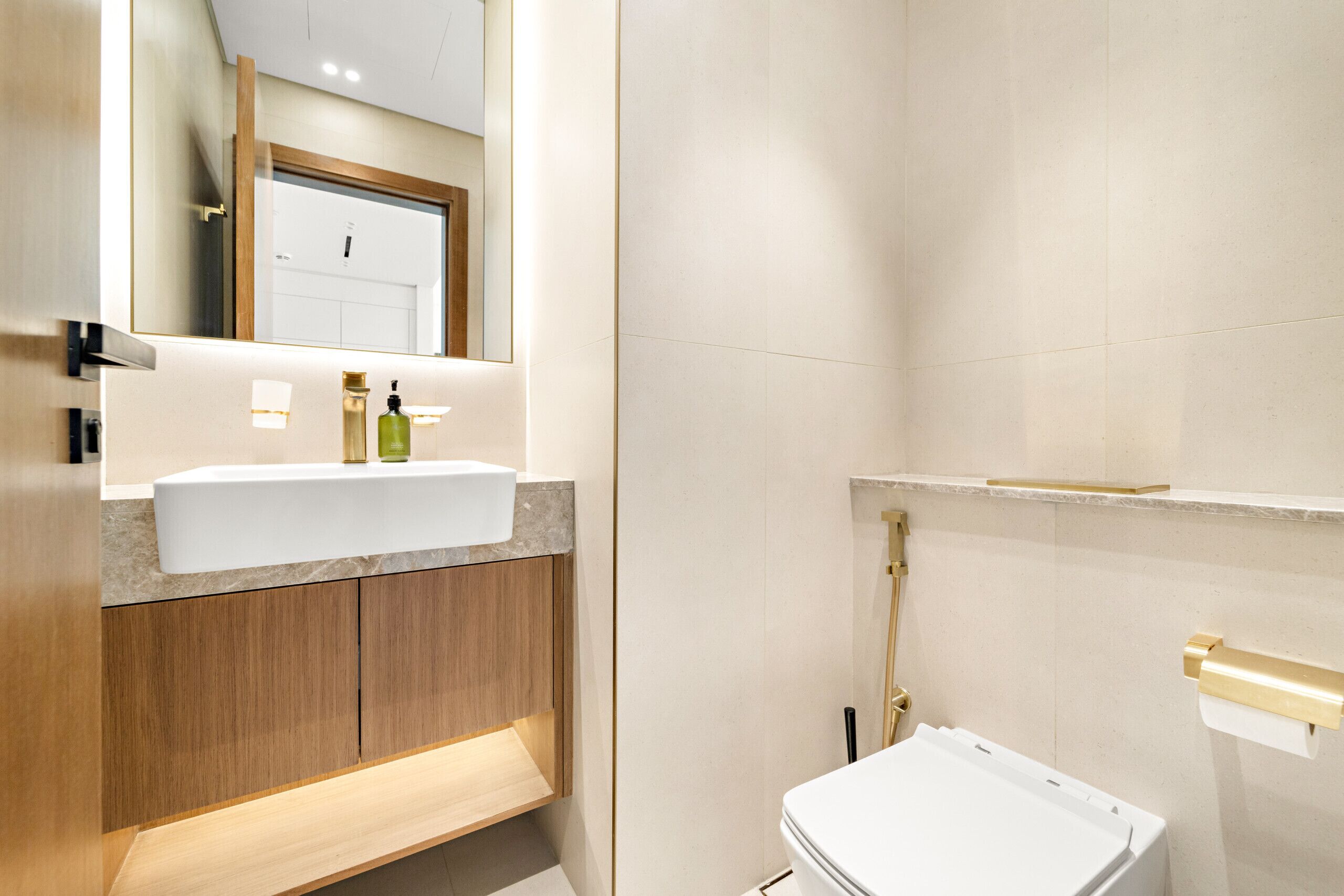 Un baño moderno con un lavabo blanco, armarios de madera, un espejo grande y un inodoro.