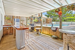 Um pátio ao ar livre com piscina, deck de madeira, área de bar e uma estátua.