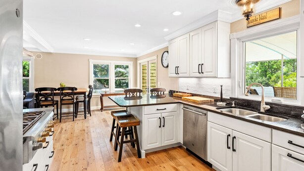 A modern kitchen with white cabinets, a central island, and a large window offering a view of greenery.
