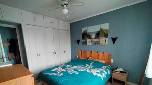 A bedroom with a bed, a wardrobe, a ceiling fan, and a wall-mounted picture.