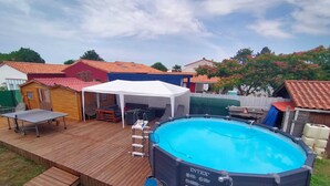 An outdoor swimming pool with a wooden deck, a covered seating area, and a small shed.