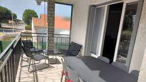 A balcony with a table and chairs, a view of the street, and a building with a tiled roof in the background.