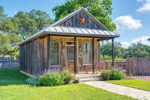 A rustic wooden cabin with a metal roof, a star decoration, and a stone pathway leading to the entrance. - Miss Thelma's | Cozy Country Retreat (Fredericksburg)