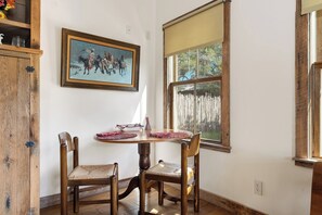 A dining area with a wooden table and chairs, a painting on the wall, and a window with a view of a fence.