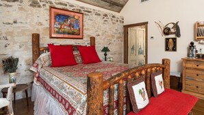 Un dormitorio rústico con pared de piedra, estructura de cama de madera y un cuadro sobre la cama.
