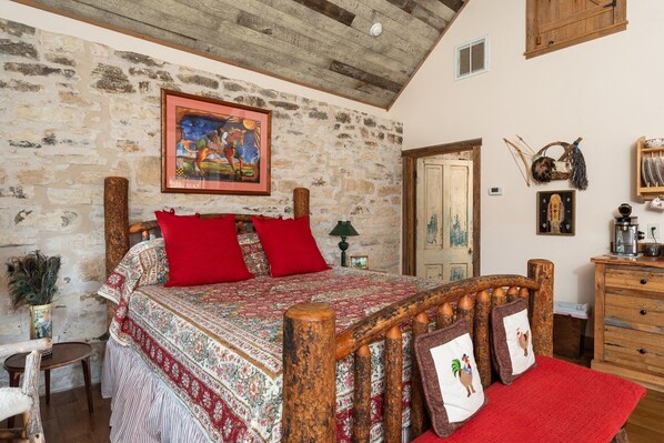 A rustic bedroom with a stone wall, a wooden bed frame, and a painting above the bed.