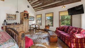 Un interior rústico con techo de madera, un sofá, un tapete de cuero de vaca y un comedor con mesa y sillas.