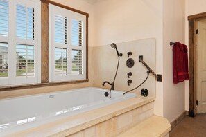A bathroom with a large bathtub, a shower with a handheld showerhead, and a towel rack with a red towel.