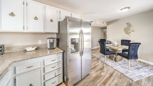 Una cocina moderna con muebles blancos, un refrigerador de acero inoxidable y una zona de comedor con mesa y sillas.