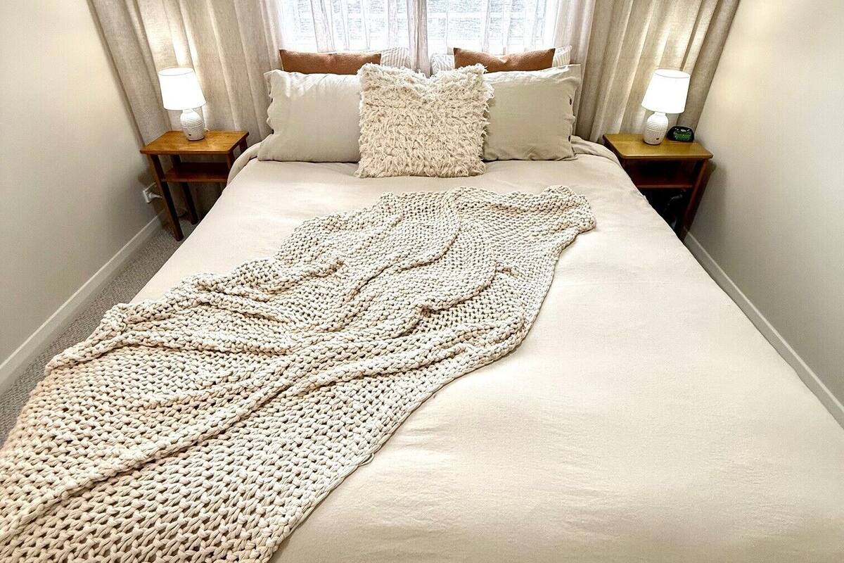 A neatly made bed with a knitted throw, two bedside lamps, and a window with curtains.