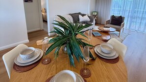 Un coin repas avec une table ronde en bois, dressée pour quatre personnes, une plante en pot et un luminaire suspendu moderne.