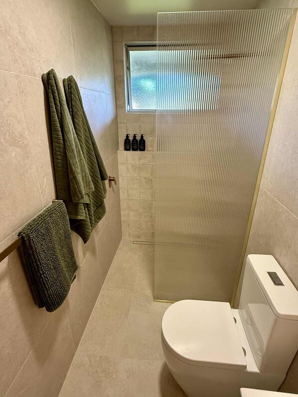 Un baño moderno con inodoro, cabina de ducha de vidrio y toallero con toallas verdes.