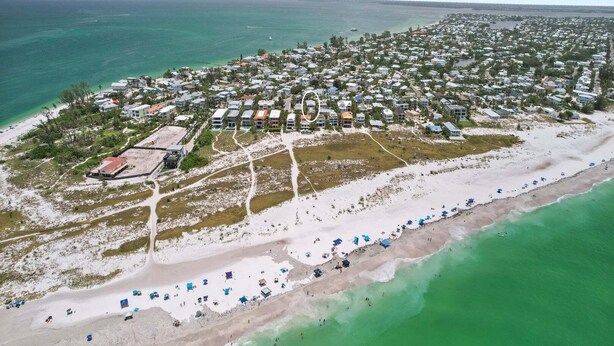 Vue aérienne d’une zone résidentielle côtière, avec des maisons, une plage et un port de plaisance.