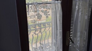 Une fenêtre ornée de rideaux en dentelle, d’où l’on aperçoit la ville.