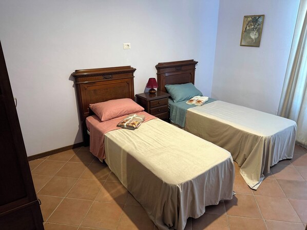 A bedroom with two single beds, a nightstand, a lamp, and a painting on the wall.